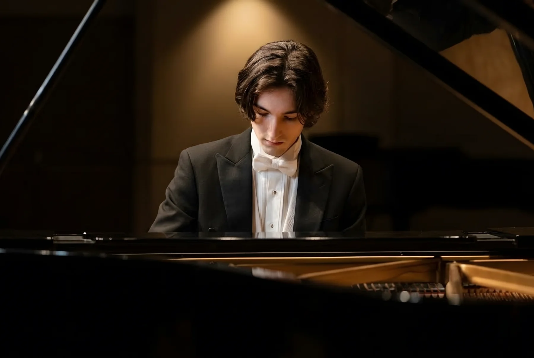 Cade at a concert grand piano in white tie, head bowed over the keys
