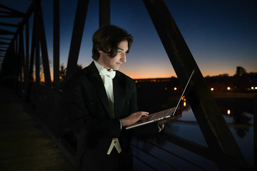 Cade working on a laptop on a bridge at dusk