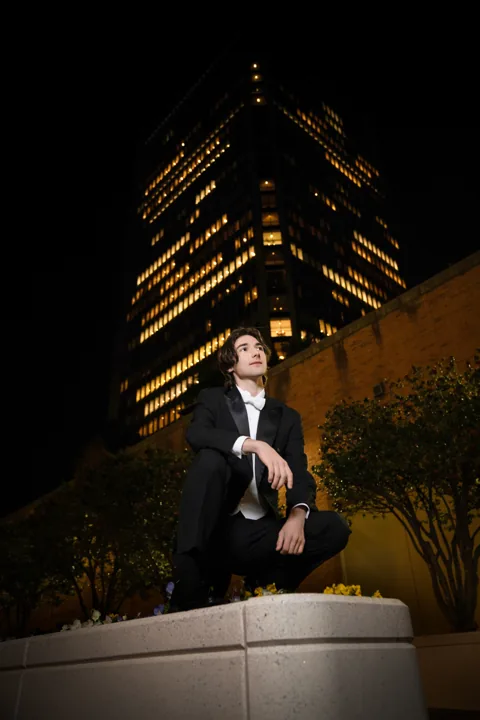 Cade in a tuxedo in front of lit city towers